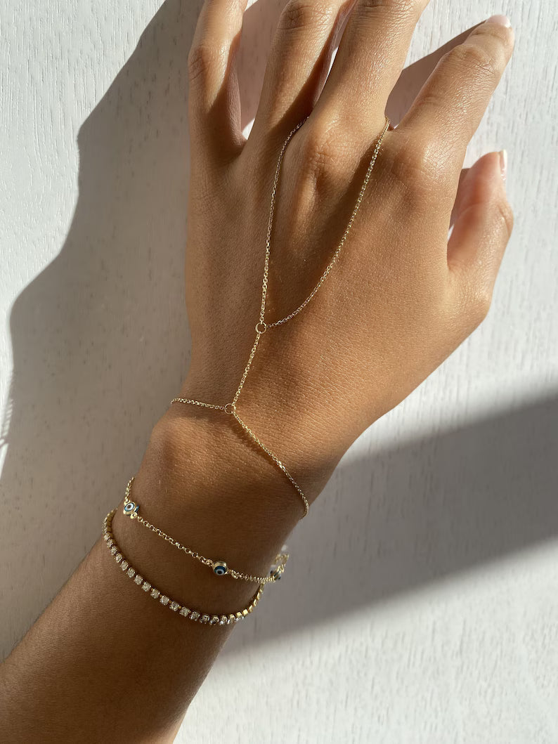Gold Vertura hand chain worn with two thin gold bracelets in soft sunlight