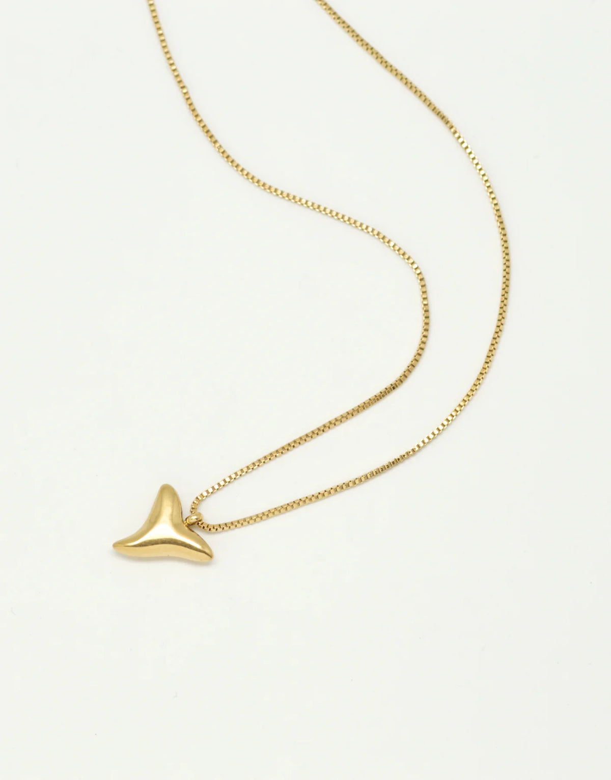 Gold shark tooth pendant necklace on a neutral background